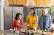 © wavebreak3 - Three female friends plus senior prepping and sipping wine at kitchen island with cutting board