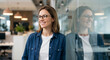 © mamo studios - Smiling confident businesswoman wearing glasses standing by a glass wall reflection in a modern corporate office interior