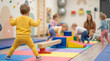 © FrameFlow - Toddler in yellow tracksuit, standing on colorful foam mats, watching children play, indoor gym daycare center, lifestyle
