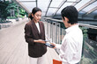 © tigercat_lpg - Young Asian smart businesspeople exchange digital contact information with NFC QR code, wireless mobile phone app technology, contactless startup collaboration at outdoor workplace, modern lifestyle.