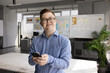 © fizkes - Portrait of young 25s smiling man with Down syndrome standing alone in modern office, using smartphone. Inclusion, accessibility, digital technology and equal opportunities for people with disability