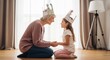 © Ariestia - Happy Grandmother and Little Granddaughter Wearing Paper Crowns Playing Together at Home