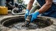 © Masque - Professional worker using a hose and gloves to extract sewage from a septic tank opening.