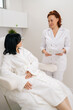 © dikushin - Vertical portrait of friendly cosmetologist holding paper document during consultation with female patient in beauty clinic. Beautician discussing treatment with woman before cosmetic procedure.