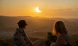 © sirbouman - Two women friends in summer dresses looking at a spectacular partial solar eclipse at sunset from Monte Toro viewpoint in Menorca, Spain