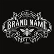 © rina - Vintage honey bee logo design element with ornate filigree frame and ribbon banners on a dark background, perfect for organic farm branding, product labels, or retro packaging.