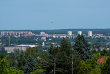 Wiosenna panorama Ostrowca Świętokrzyskiego w Polsce, prezentująca połączenie elementów miejskich i naturalnych. W tle dominują średniowysokie budynki mieszkalne, przeplatane drzewami i zielenią. 