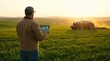 © farid - Rear view of smart farmer holding digital tablet with data graphics while managing autonomous tractor in green agricultural field at sunset