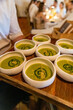 © giemmephoto - Chef serving elegant green vegetable soup appetizers on a wooden tray in a fine dining restaurant, with warm ambient lighting and guests blurred in the background.