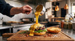 © Adrian - Chef pouring melted cheese sauce over open burger in kitchen
