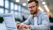 © lililia - Smiling businessman using laptop in modern office, online business communication concept.