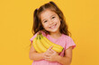 © Сергей Стельченко - A young girl stands in front of a yellow backdrop. She holds a bunch of bananas close to her chest. Her smile shows joy and excitement in the moment.