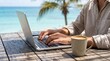 © MT - Digital nomad man working on laptop at beach cafe table with coffee, remote work lifestyle concept, freelance professional typing on computer outdoors