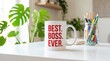 © Mudassir - White ceramic coffee mug featuring bold red text that says best boss ever sitting on a clean modern office desk