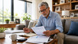 © Thodsapol - Senior man reviewing bills and financial documents at home, managing expenses, budgeting, retirement planning, and personal finances.