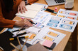 © wattana - UX designer working on mobile app wireframes with markers, notebooks, and printed interface layouts on a desk.