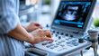 © Nataliya - Close-up of an ultrasound machine displaying a fetal image with an anonymous hand operating the controls, medical technology and prenatal care concept, faceless, defocused, with