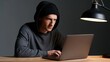 © AZ Studio - Focused man in hoodie typing on laptop in dimly lit room with desk lamp
