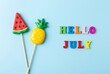 © Pixels Stock - Hello July candy lollipops pineapple watermelon and colorful alphabet blocks spelling word july on light blue background summer vacation fun.