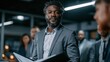 © Farah - Confident african american male executive holding a document while standing in a modern corporate office setting
