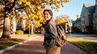 © Rendara Studio - Engaged college student walking on autumn campus path with backpack near old buildings