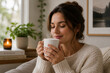 © mila103 - Young woman savoring hot drink while seated in living room