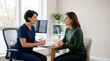 © Xenia - Female doctor consulting with patient in clinic office. Smiling healthcare professional in blue scrubs talking to woman during medical appointment