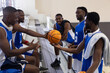 © wavebreak3 - African American men basketball players in blue white jerseys sitting on bench passing orange ball