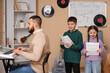 © Pixel-Shot - Music teacher playing electronic piano with two happy children singing from sheet music in a home studio