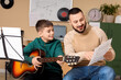© Pixel-Shot - Young boy learning guitar with male teacher, music education and skill development, private lesson in a classroom setting