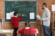 © Pixel-Shot - Young boy learning music theory on chalkboard with teacher and classmates in a modern classroom setting, music education and childhood development are central themes