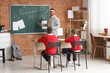 © Pixel-Shot - Music teacher explaining musical staff to young students in classroom with instruments and chalkboard, the instructor points to the chalkboard with musical notation