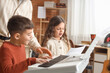 © Pixel-Shot - Young children learning piano and singing with teacher, music education and creative development for kids, the boy plays the keyboard while the girl sings from sheet music
