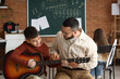 © Pixel-Shot - Young boy learning acoustic guitar from male teacher in music class, educational development and creative skill acquisition
