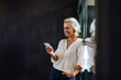 © Westend61 - Smiling casual mature businesswoman using smartphone at the window in loft office