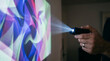 © baiti - Hand holding compact projector casting vibrant abstract light patterns onto a screen