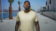 © Krakenimages.com - Man with tongue out wearing beige tshirt, standing center frame near palm trees and marina on a sunny street promenade; playful confidence.