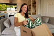 © Home-stock - Young woman happily removing new clothing item from cardboard package, enjoying arrival of order while sitting on sofa at home