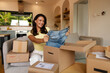 © Home-stock - Female shopper holding up pair of jeans and smiling with satisfaction while unpacking online purchases, surrounded by cardboard boxes