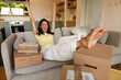 © Home-stock - Excited woman sitting on sofa surrounded by many delivery parcels and raising hands in winner gesture, celebrating arrival of online shopping orders