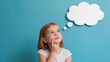 © Ирина  - Young girl with short blonde hair looking up thoughtfully against a blue background, a white speech bubble above her head suggesting imagination or contemplation