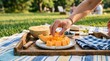 © Olga Ко - Female hand taking a piece of fresh cantaloupe melon from a plate. Aesthetic summer outdoor picnic on a wooden tray in a sunny park.