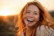 © Natallia Simanchyk - A redheaded woman with freckles laughs joyfully outdoors. The warm sunset light creates a golden atmosphere. Perfect for lifestyle, happiness, or beauty advertisements.