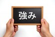 © Jumpei - 「強み」と書かれた黒板を両手で掲げるビジネスシーンで自己分析を表現