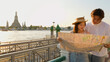 © blueringmedia - Asian Couple Reading Paper Map by Chao Phraya River at Sunset