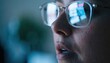 © thanawat - Close-up of a person wearing glasses reflecting a computer screen, focusing intensely on the digital content in a dimly lit environment.