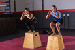 © wavebreak3 - Two female fitness trainees balancing on wooden plyometric boxes on red mat, wearing sportswear