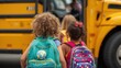 © Dream Studio - Rear view of young children with colorful backpacks walking towards a yellow school bus on a cloudy morning day