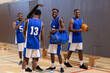 © wavebreak3 - African American male team in blue white jerseys holding orange basketball and duffel in gym