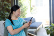 © wavebreak3 - Mature woman teal-shirt sitting on armchair by glass doors holding phone leaning on green pillow
